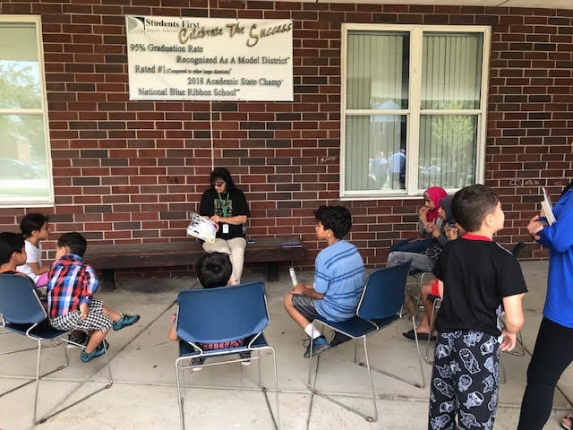 Teacher sitting on a bench reading to students.
